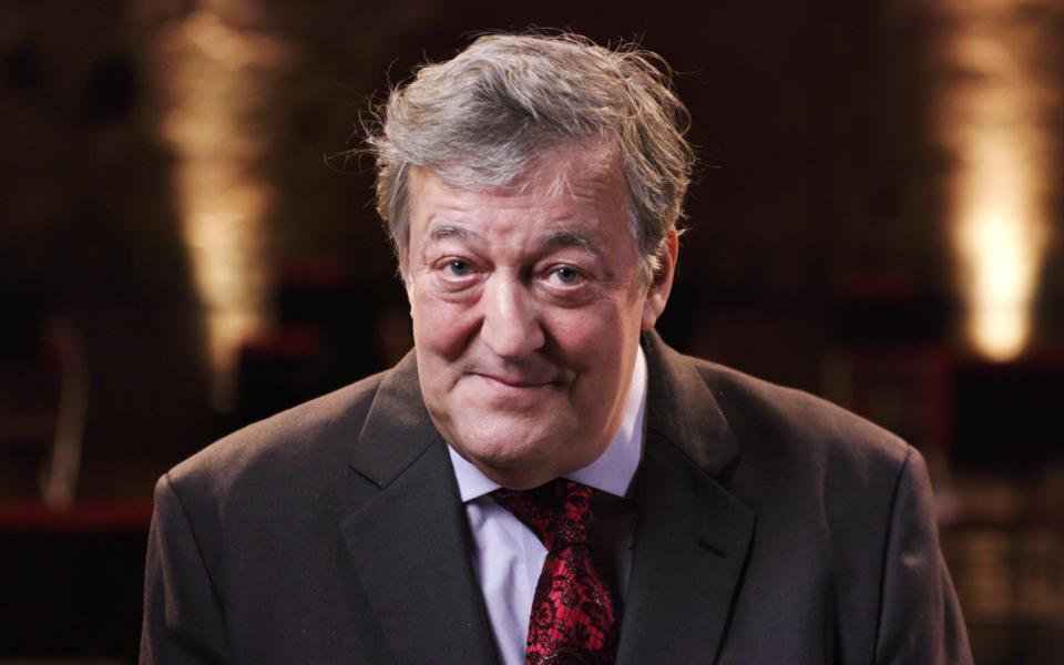 Stephen Fry looking at camera, wearing coat and red tie