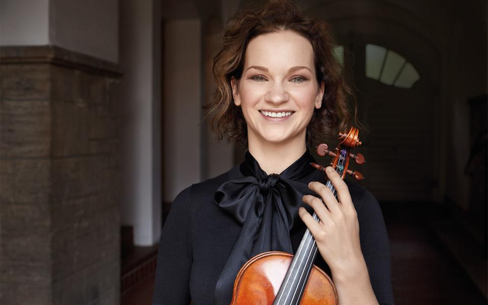 Violinist Hilary Hahn in black blouse with her instrument smiling.