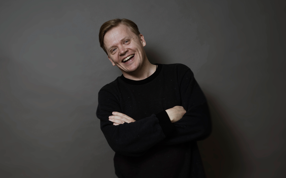 Violinist Pekka Kuusisto in black sweater smiling brightly.