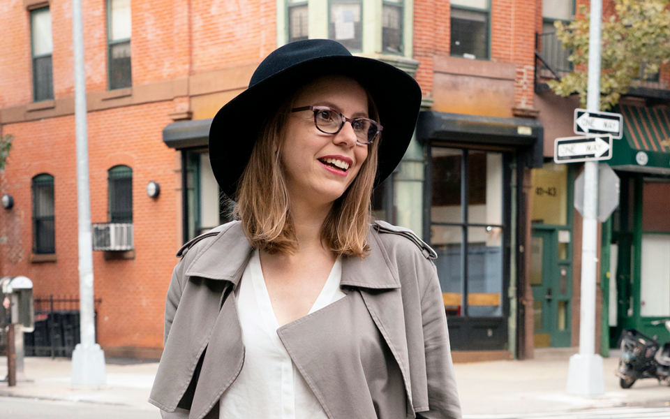 Composer Anna Clyne in beige jacket and black hat at a crossing.