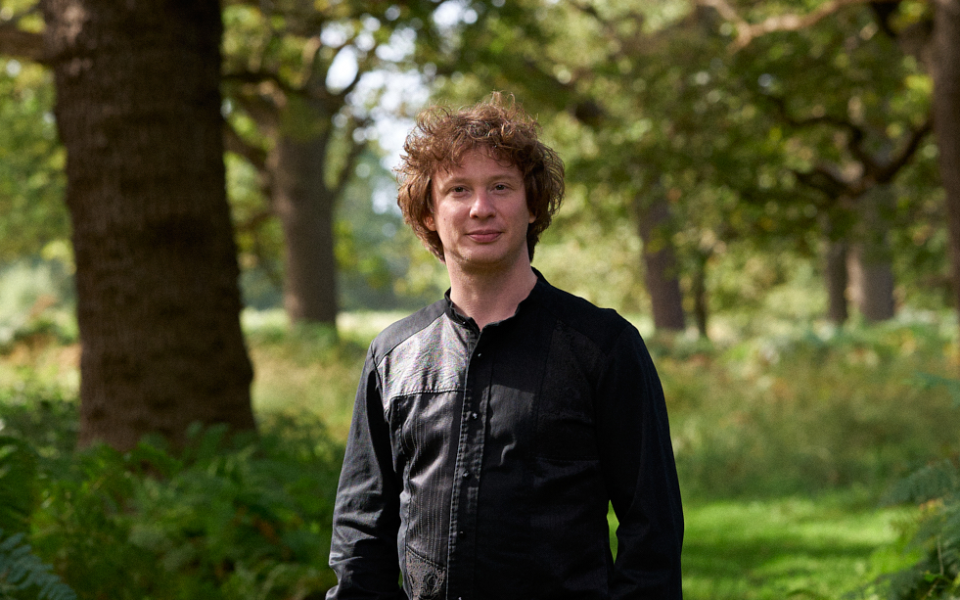 Conductor Santtu-Matias Rouvali wearing in black shirt standing amongst trees.