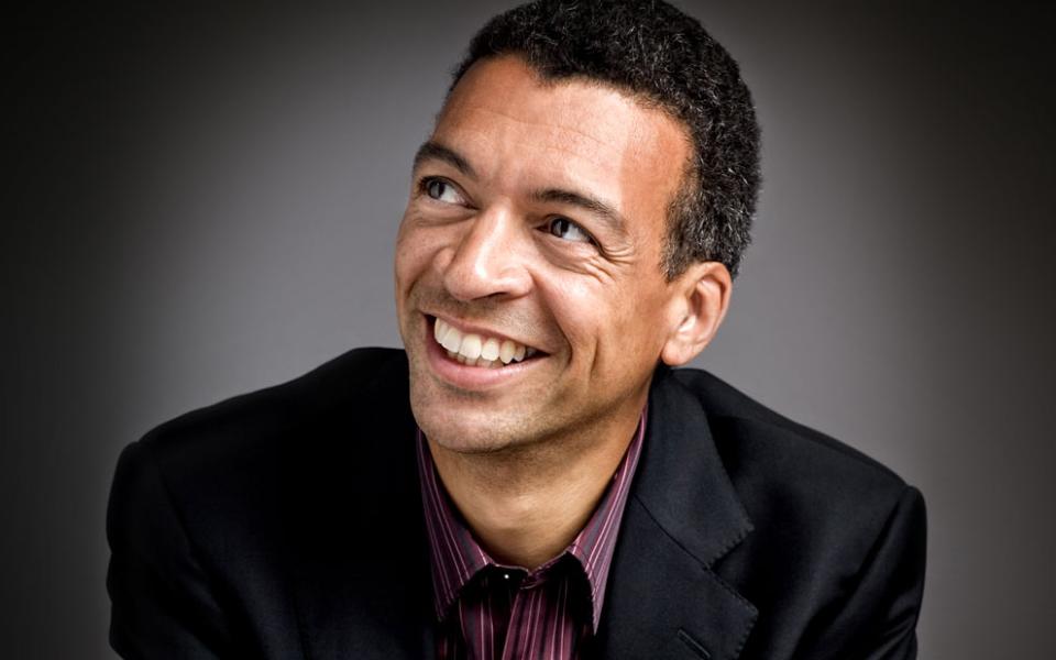 Baritone Roderick Williams in black shirt looking left smiling.