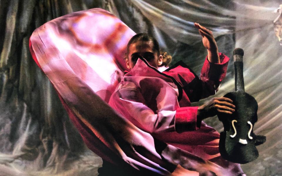 A dancer in red cape quickly moving holding a textile violin.